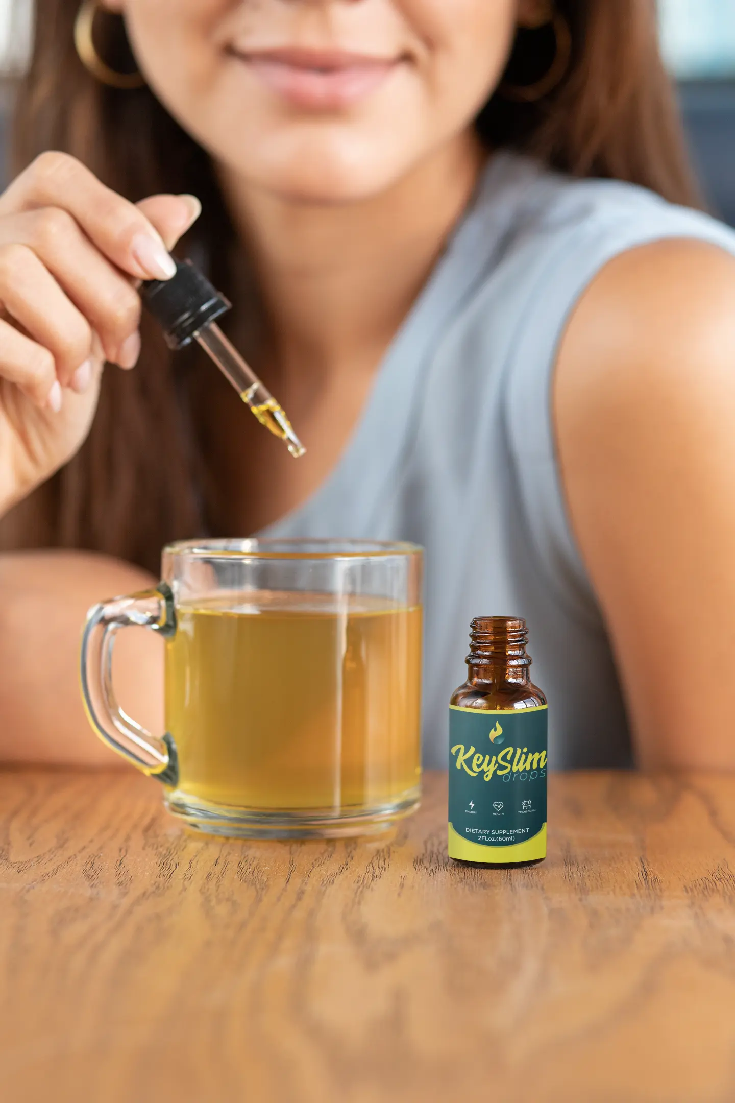 A woman using the KeySlim Drops dropper bottle for metabolic support next to a mug of natural yellow liquid.